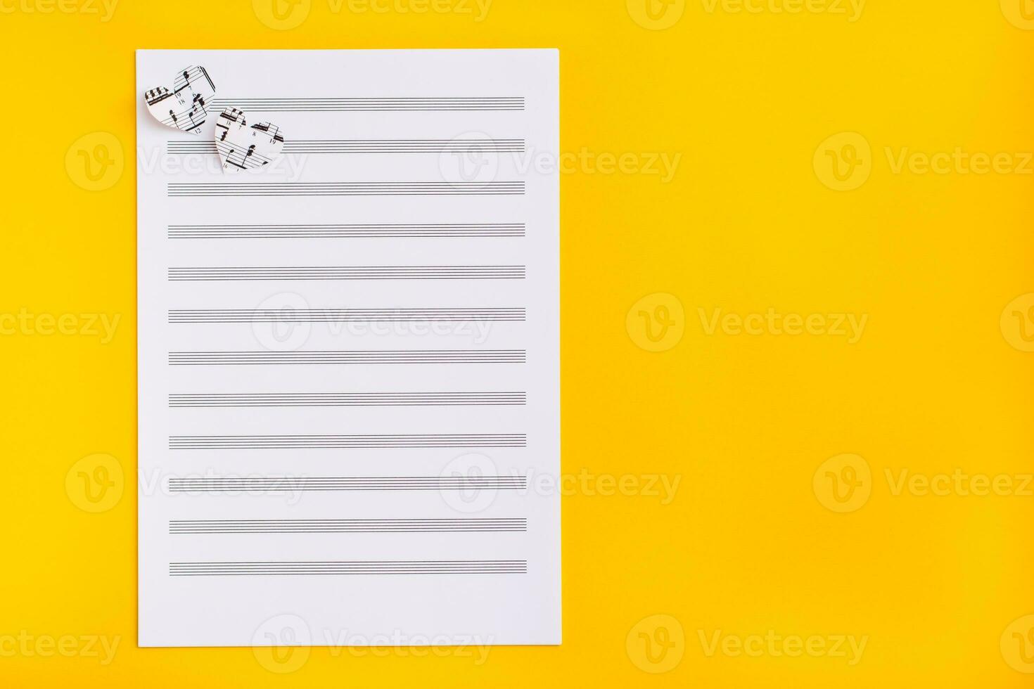 Blank sheet music and hearts cut from music text on yellow background. Top view. Copy space photo