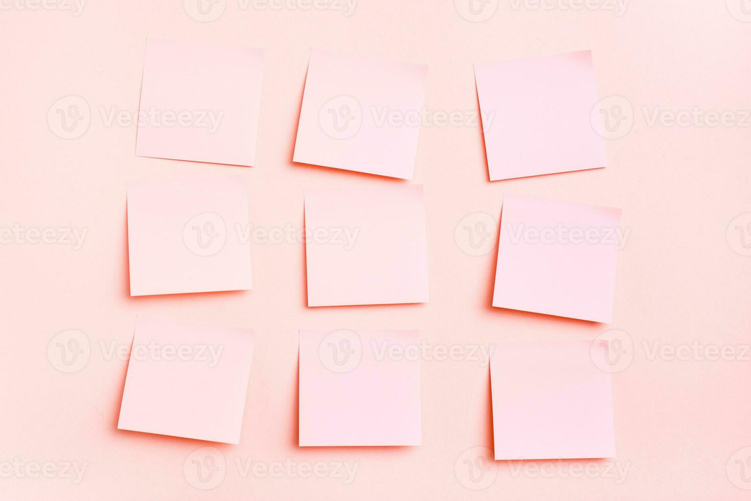 The concept is pink. Blank square small sheets of paper to write in even rows on a pink background. Top view photo