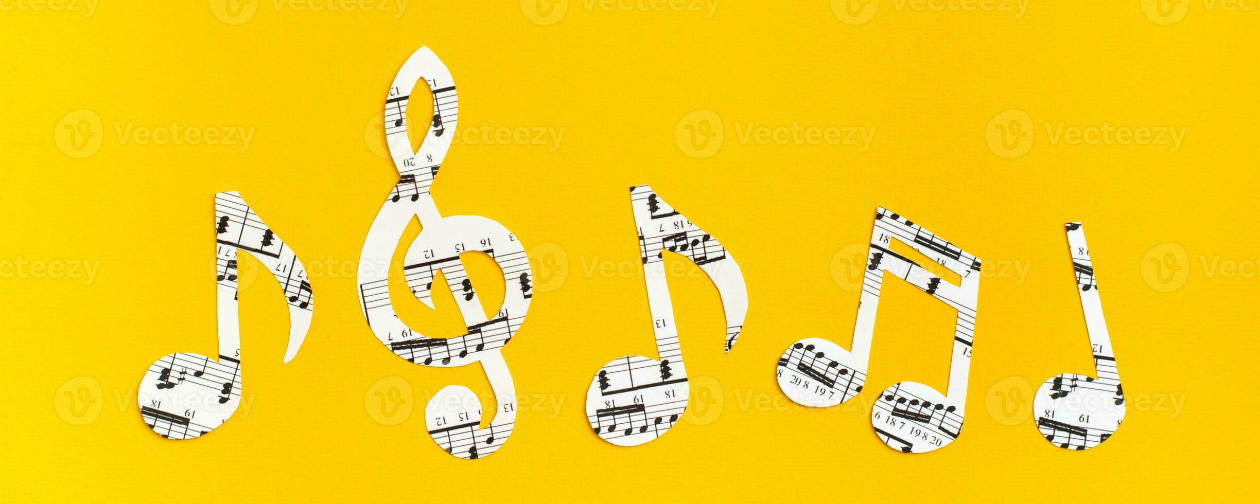 Musical notes and clef cut from paper with musical text in a row on yellow background. Web banner photo