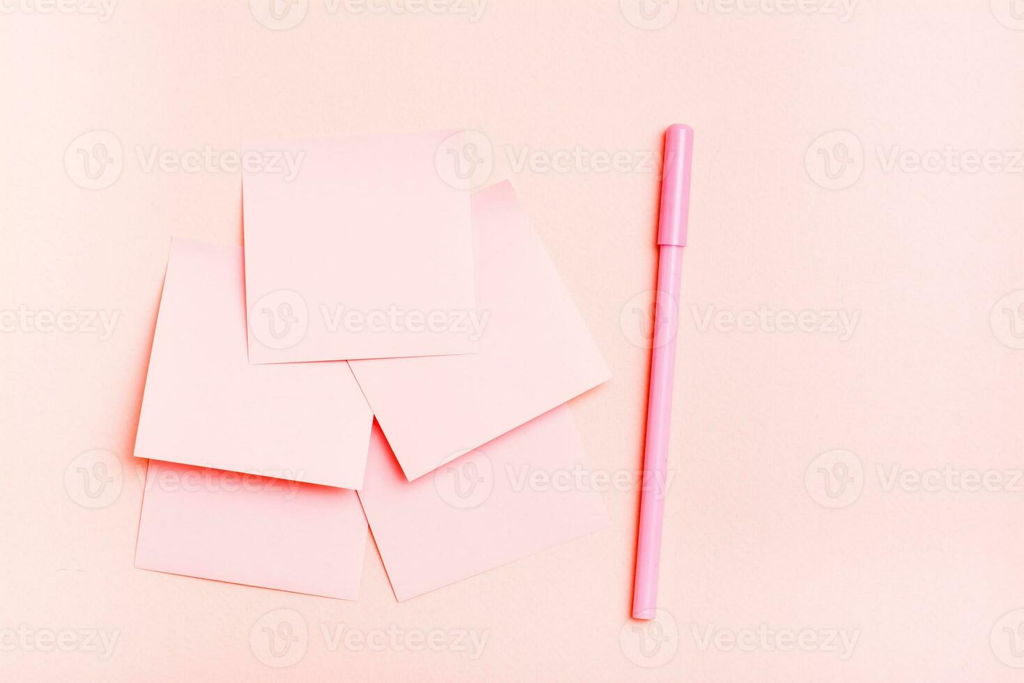 The concept is pink. Blank square small sheets of paper and a pen on a pink background. Top view photo
