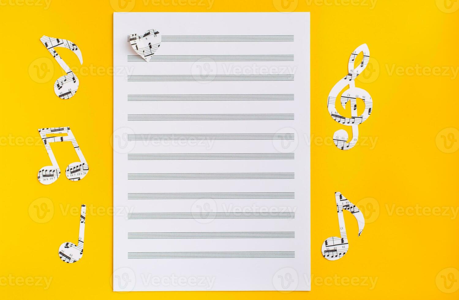 Blank sheet music, music notes and hearts cut from music text on yellow background. Top view photo