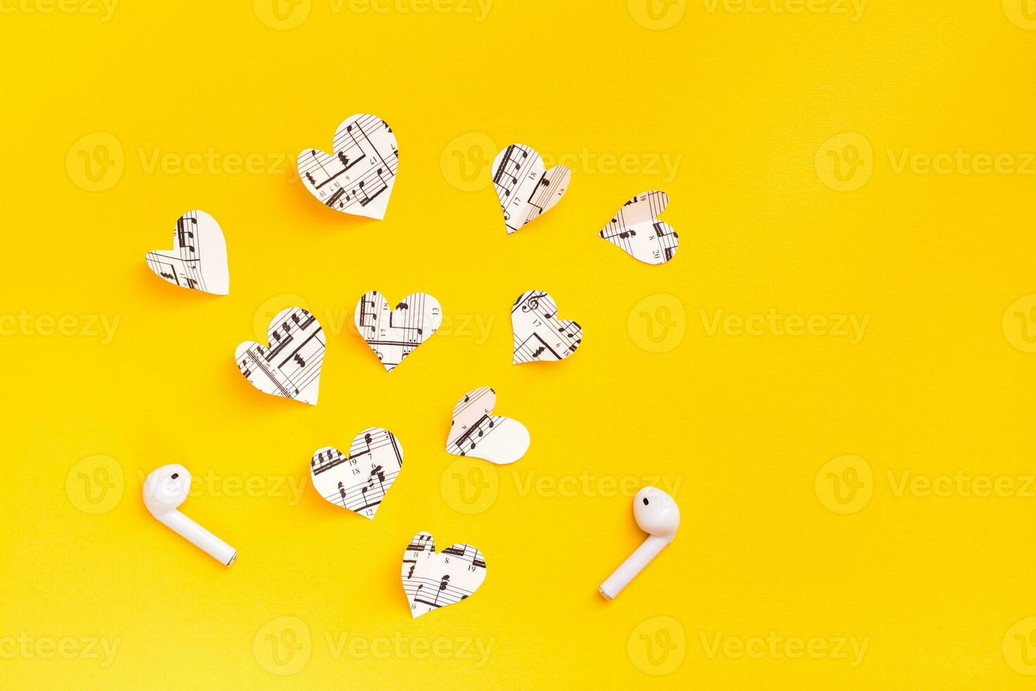 Wireless headphones and hearts cut from the music text on a yellow background. Love for music through gadgets. Copy space photo