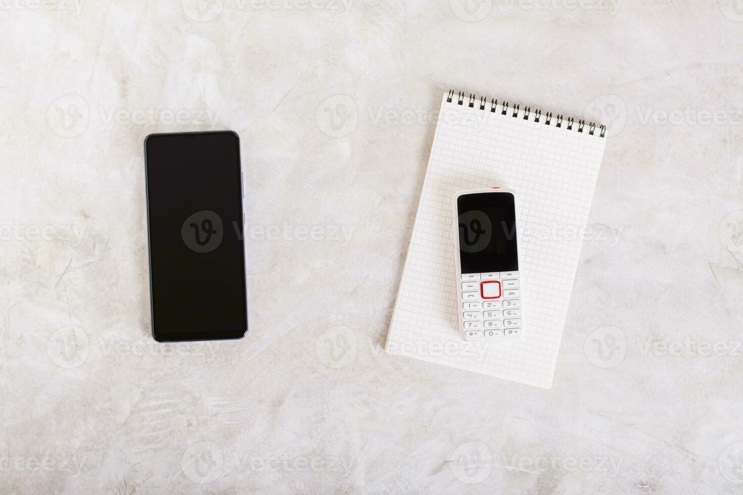 Modern smartphone and push-button phone on notepad on table top view photo