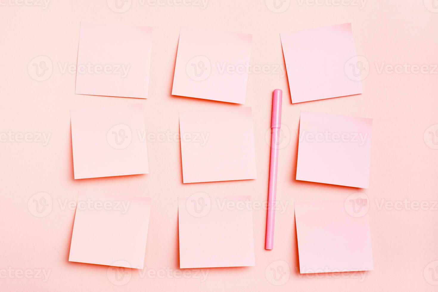 The concept is pink. Blank square small sheets of paper to write in even rows and a pen on a pink background. Top view photo