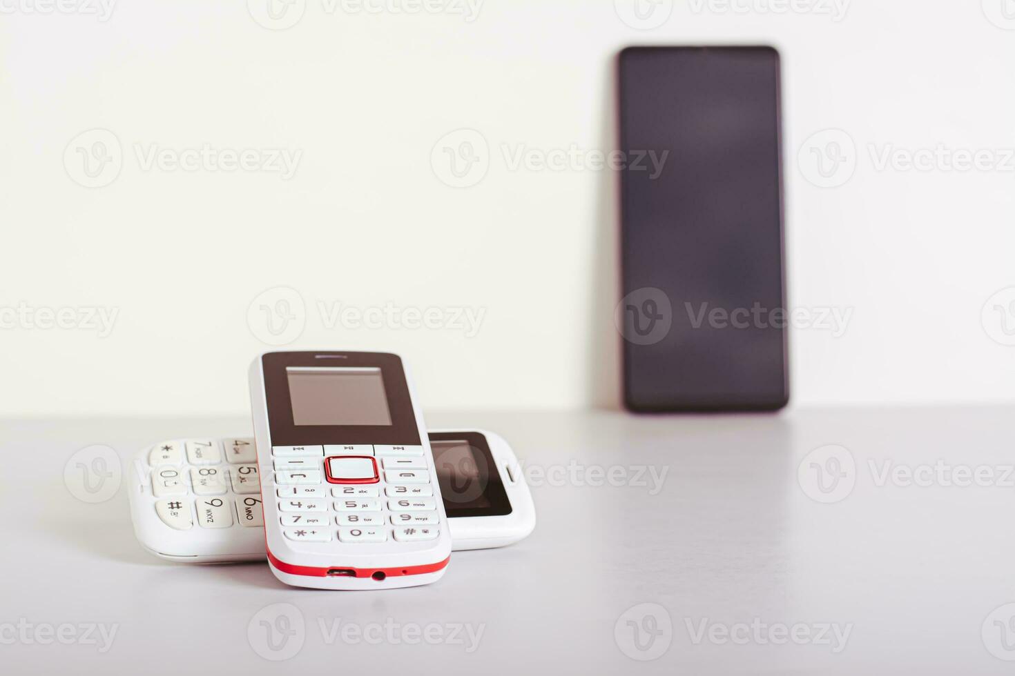 Two old-fashioned white push-button telephones lie on the table on the background of a smartphone photo