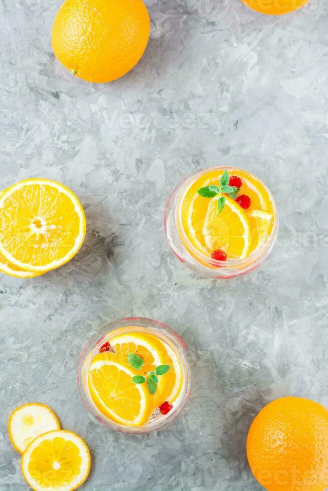 Hard seltzer cocktail with orange, cranberry and mint in glasses and cut oranges on the table. Alcoholic beverage. Vertical and top view photo