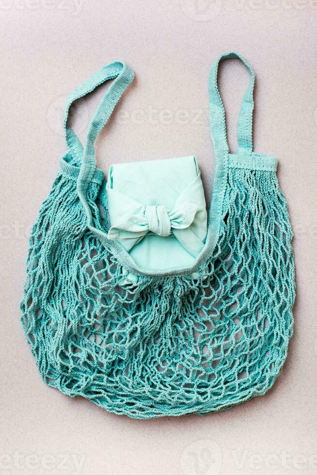 Eco-friendly gift - box wrapped in cloth in a mesh bag on a gray background. Minimalism. Blue palette photo