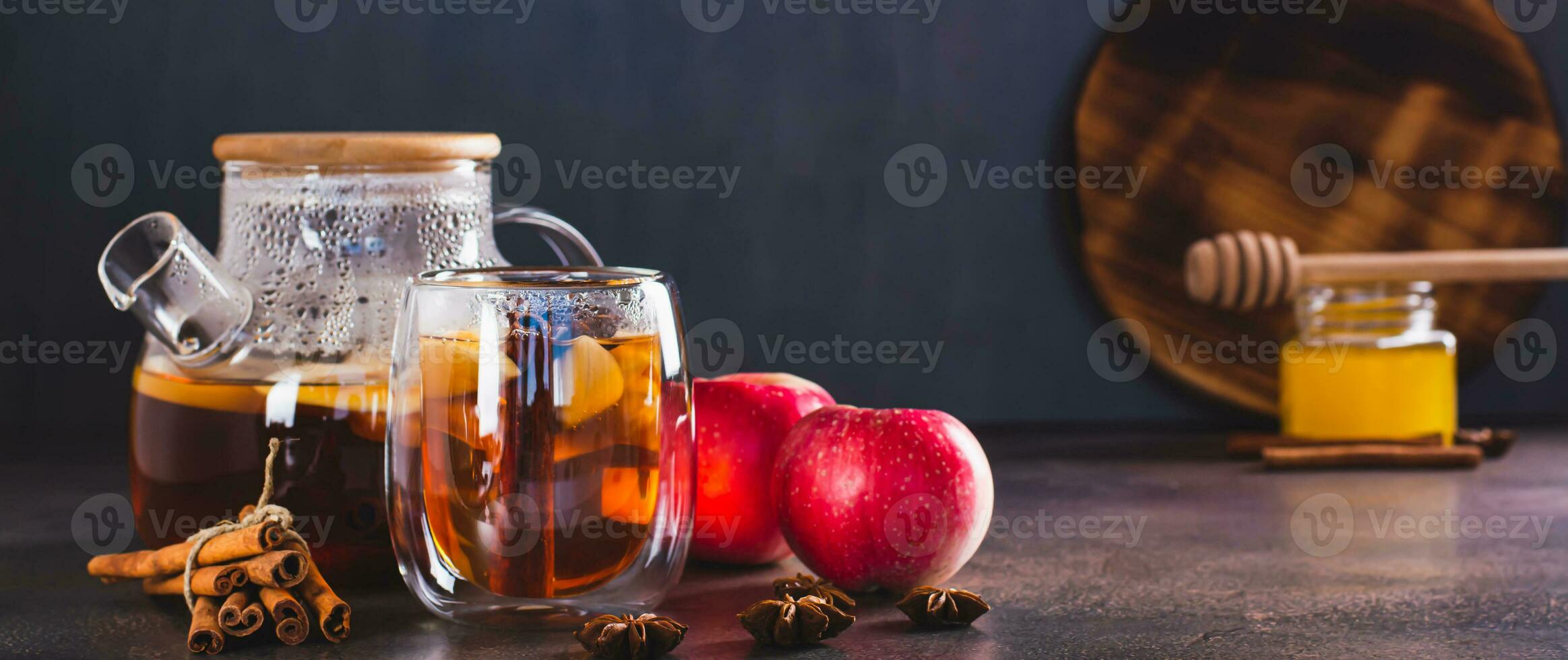 Hot tea with apples, cinnamon, star anise and honey in a cup and teapot on the table web banner photo