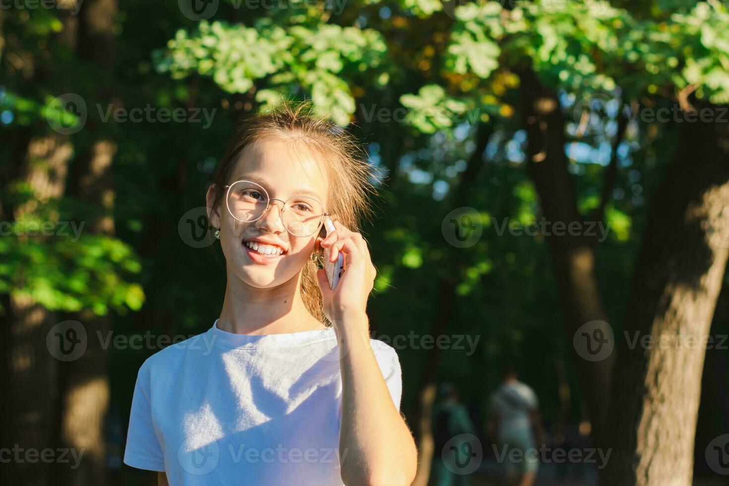 A girl in glasses happily talks on a push-button telephone among the trees photo