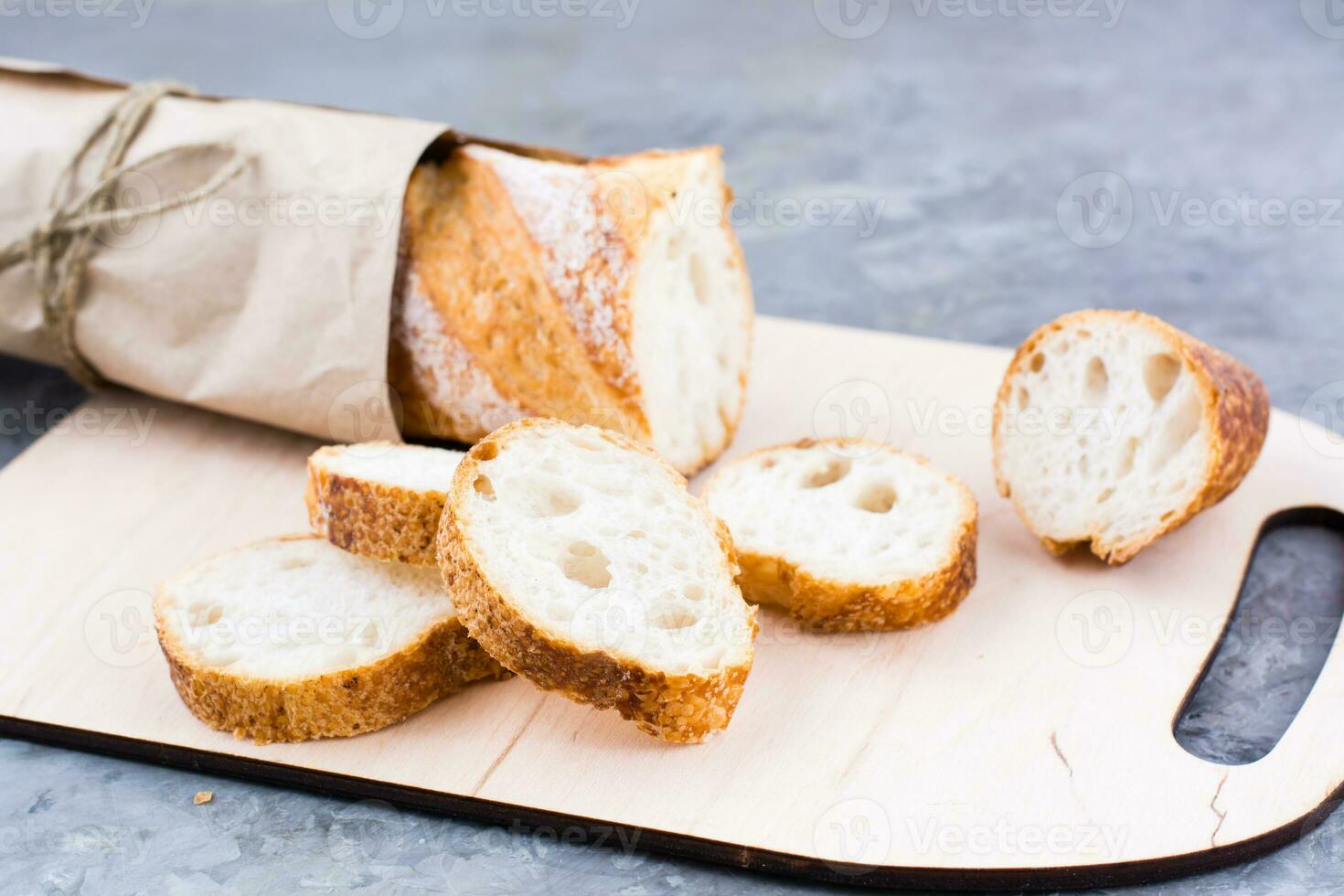 Fresh baguette in wrapping paper cut into pieces on a cutting board on a table photo