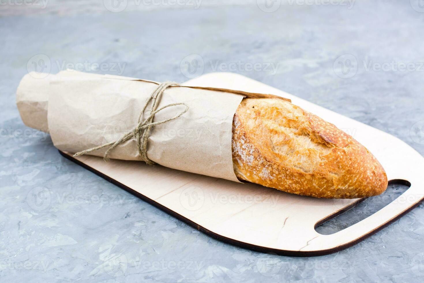 Fresh baguette in wrapping paper on cutting board on table photo