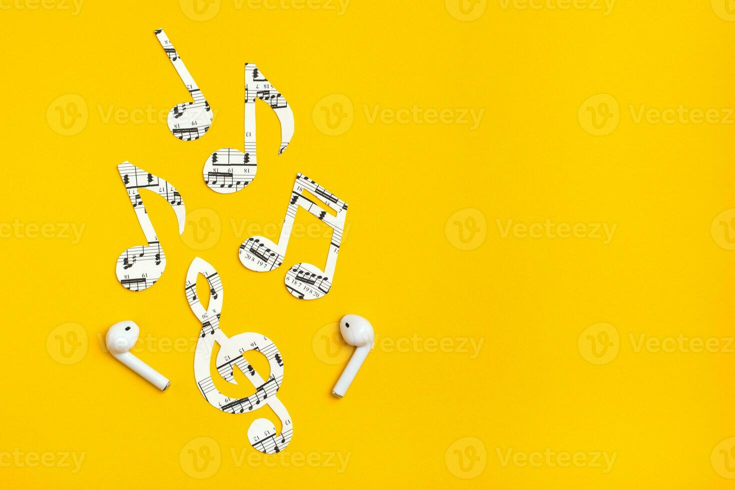Wireless headphones and music notes cut from paper on a yellow background. Music imitation concept. Copy space photo