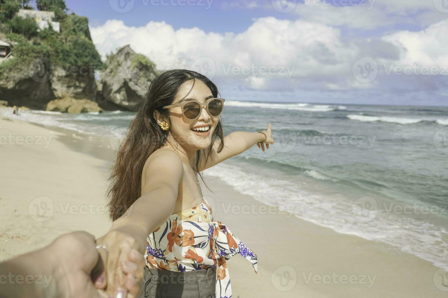 A happy young Asian woman is smiling to the camera and pointing at the beach in Gunungkidul, Indonesia. photo
