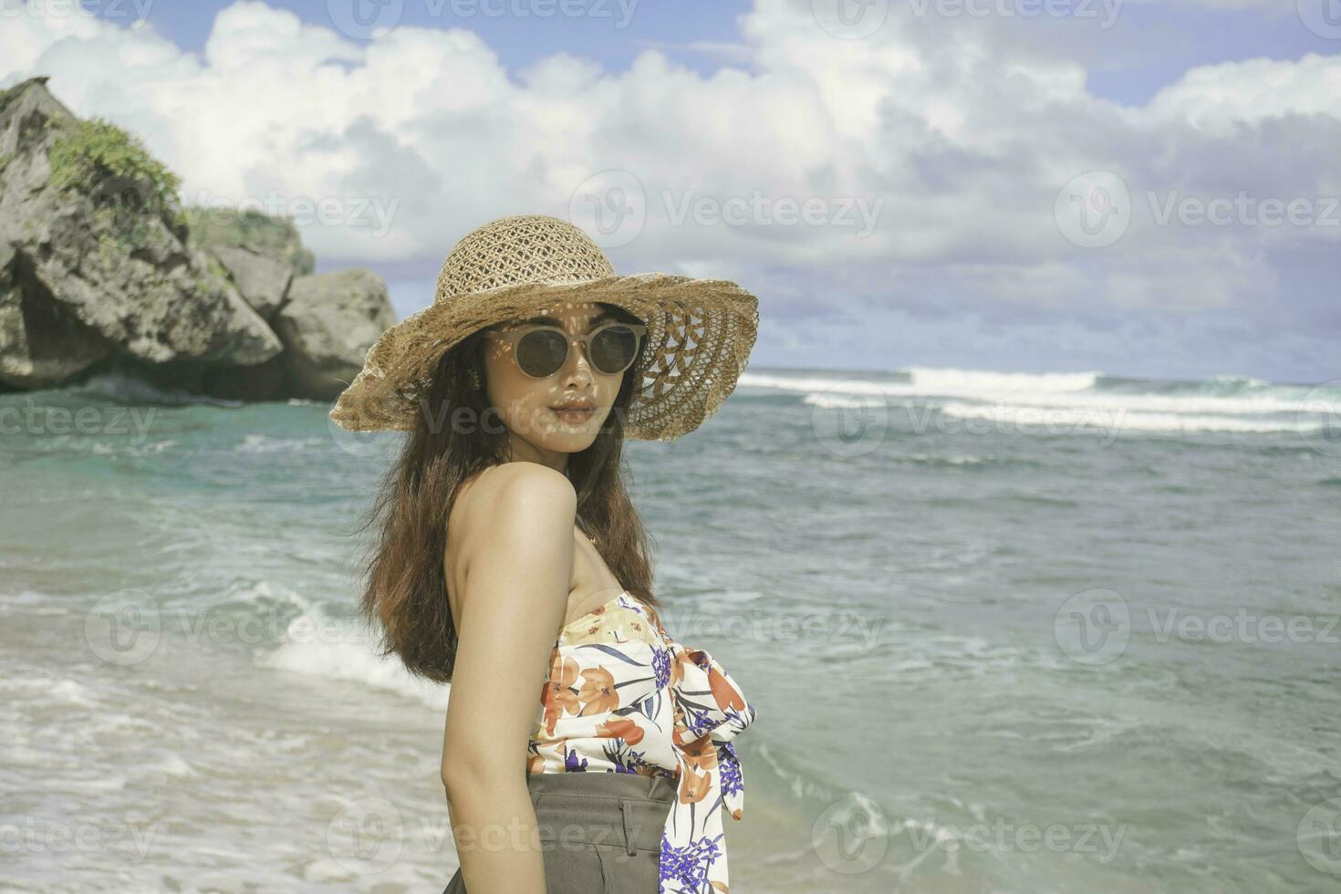 A happy young Asian woman wearing beach hat is posing to the camera at the beach in Gunungkidul, Indonesia photo