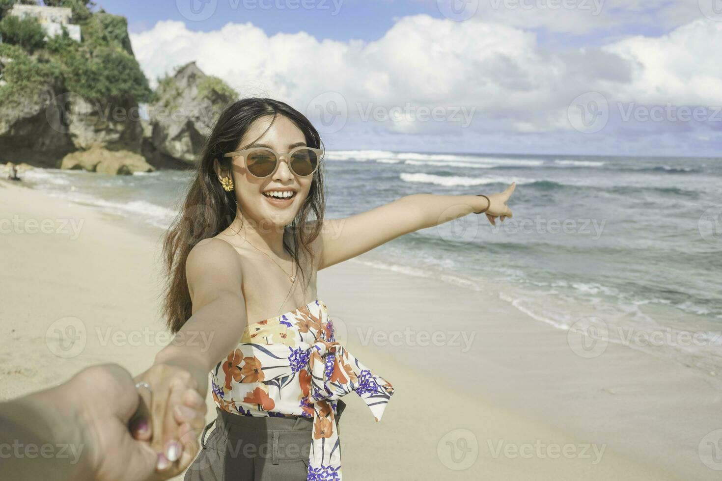 A happy young Asian woman is smiling to the camera and pointing at the beach in Gunungkidul, Indonesia. photo