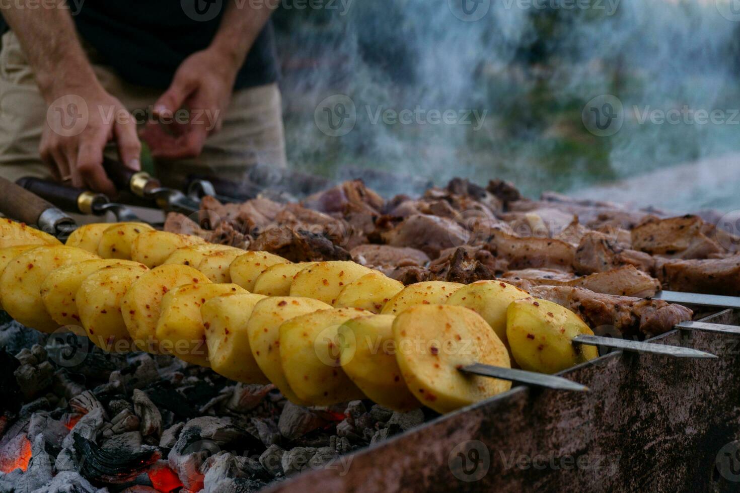 Male hands cooking meat on skewers on barbecue grill outdoors photo