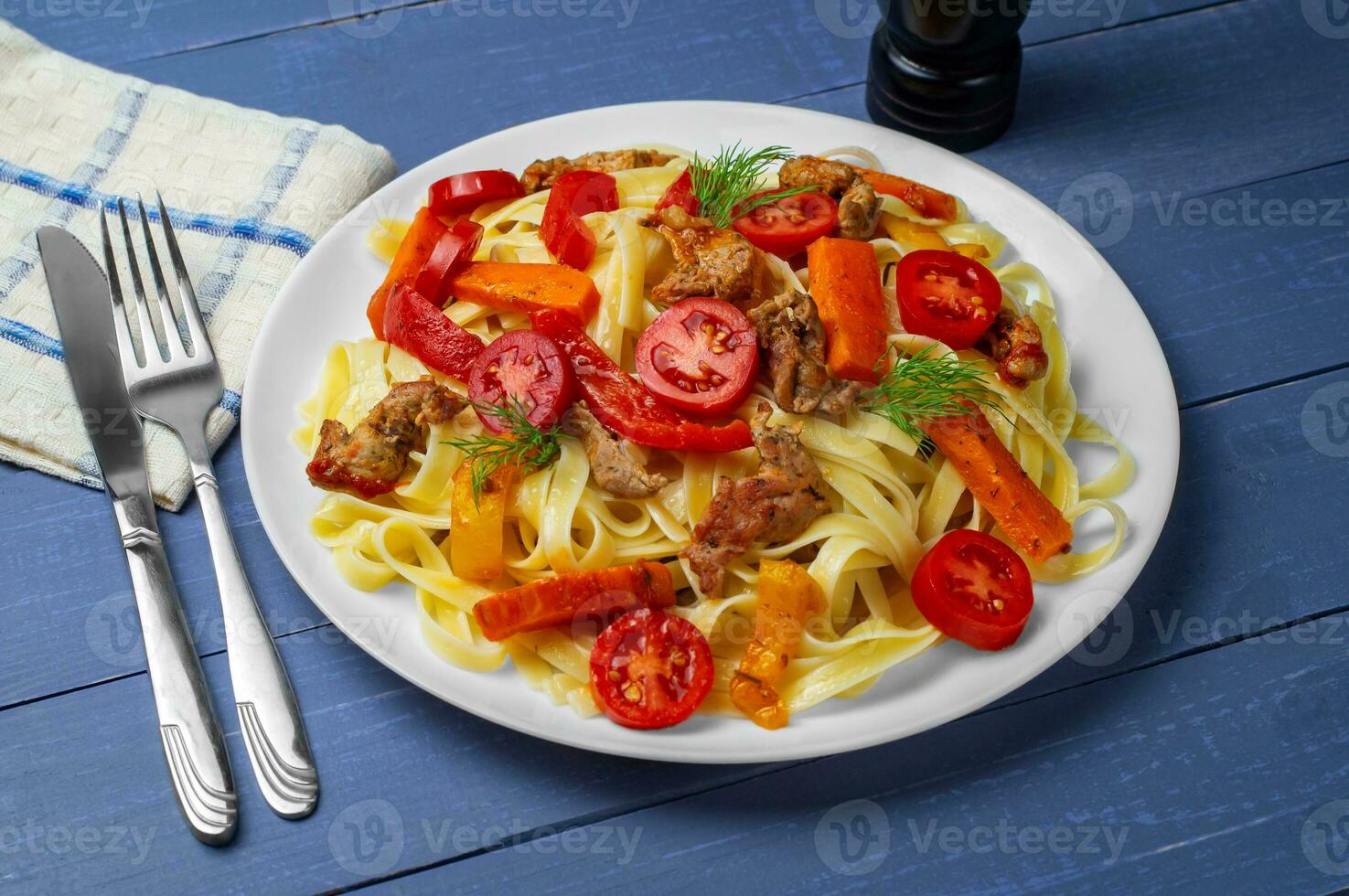 Fettuccine with grilled meat, carrots, bell peppers, dill tomatoes on a blue wooden background. Pasta with vegetables. Side view. photo