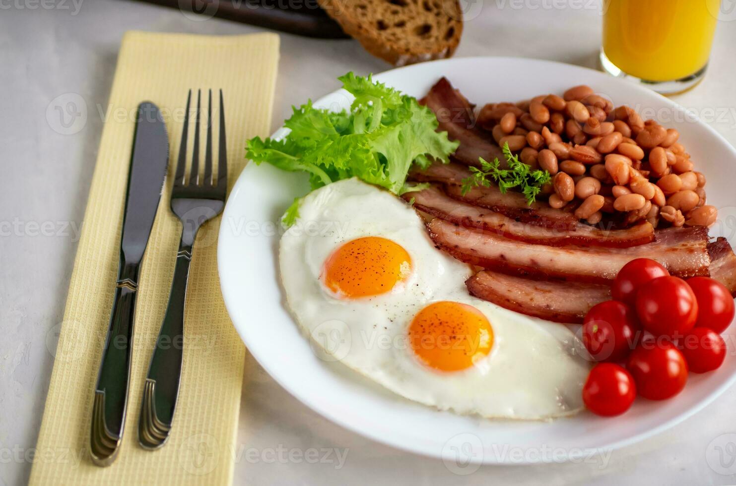 Hearty breakfast with scrambled eggs, bacon, beans, cherry tomatoes, homemade bread, orange juice on a concrete countertop. English breakfast concept. photo