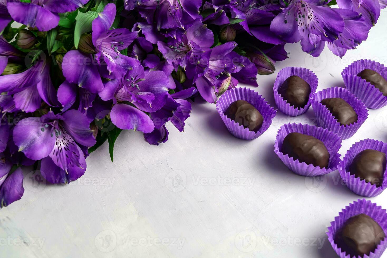 ramo de flores de Violeta Alstroemeria y un conjunto de chocolates mentiras en un hormigón antecedentes. Copiar espacio. tarjeta postal concepto. foto