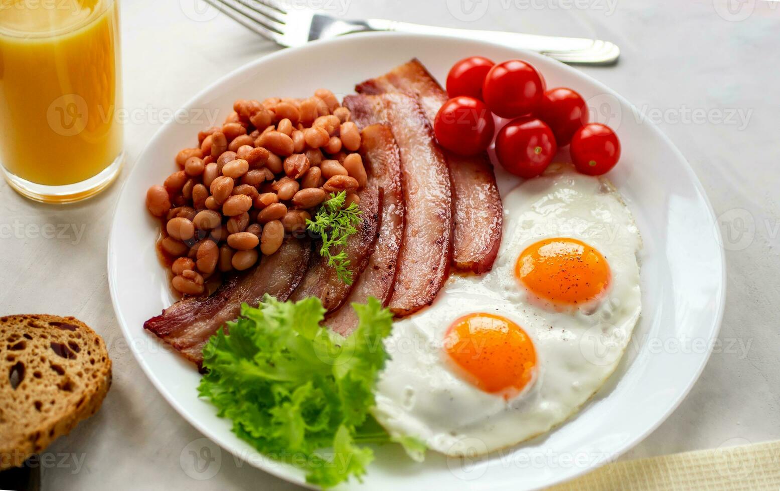 abundante desayuno con revuelto huevos, tocino, frijoles, Cereza Tomates, hecho en casa pan, naranja jugo en un hormigón encimera Inglés desayuno concepto. foto