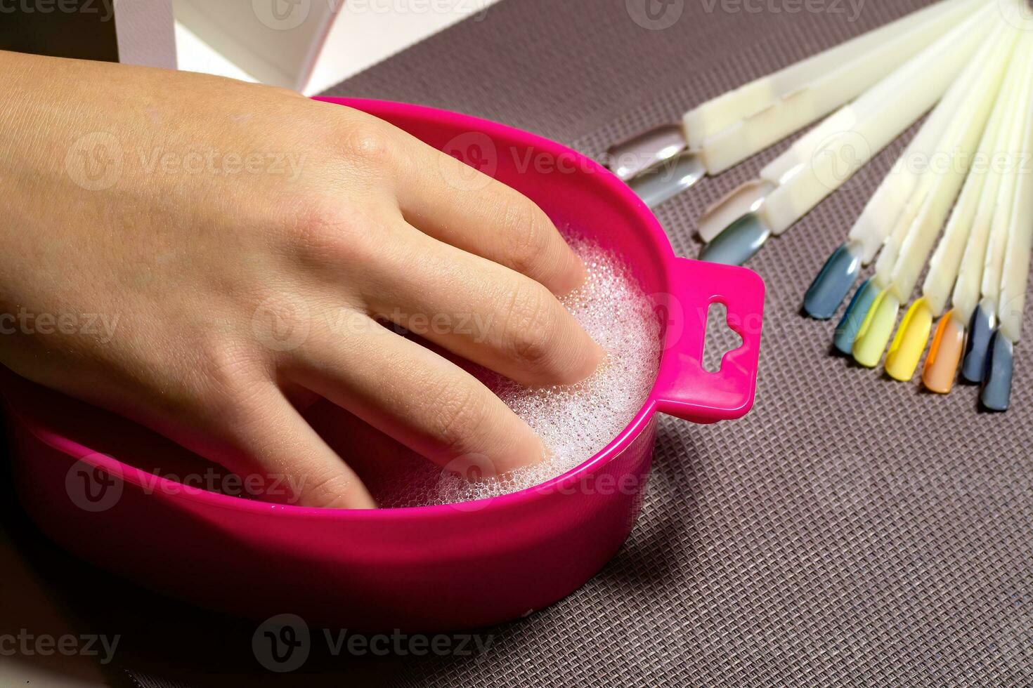 Soaking and steaming the skin of the hands with soapy water in a pink bath before performing a manicure.  Professional manicure in a beauty salon.  Hand care concept photo