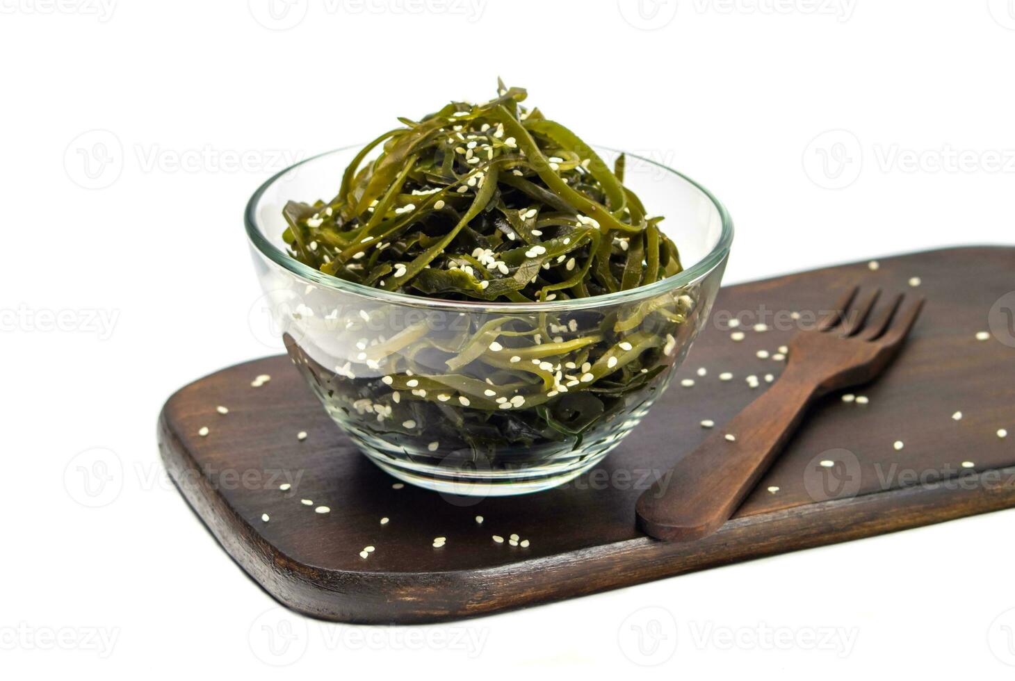 Seaweed kelp Laminaria in a glass bowl, sprinkle sesame seeds on a wooden board, Isolate on white background. Seaweed salad. Healthy food concept. photo