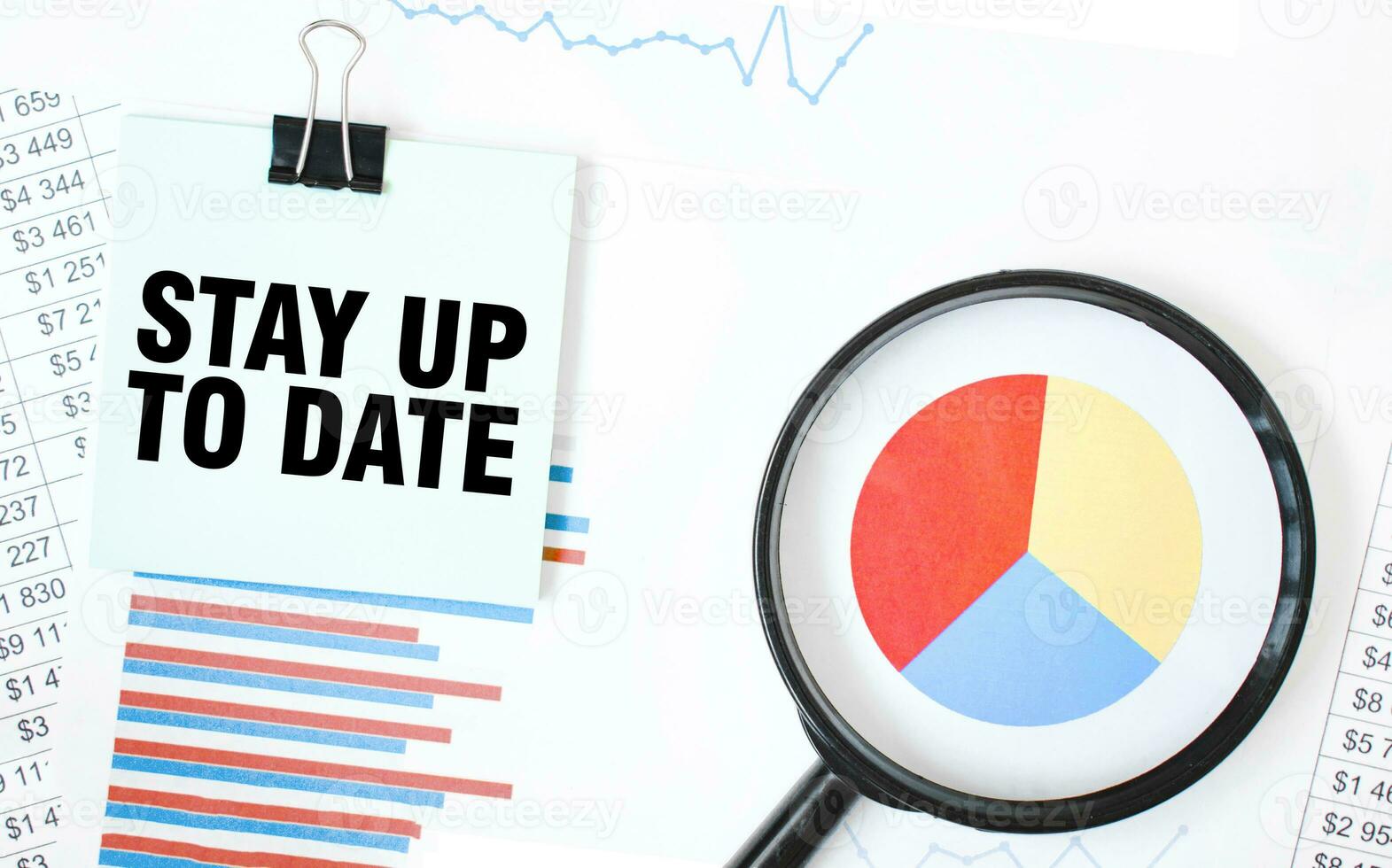 Green card on the white notepad and magnifier on the financial documentation. Text STAY UP TO DATE. Business concept photo