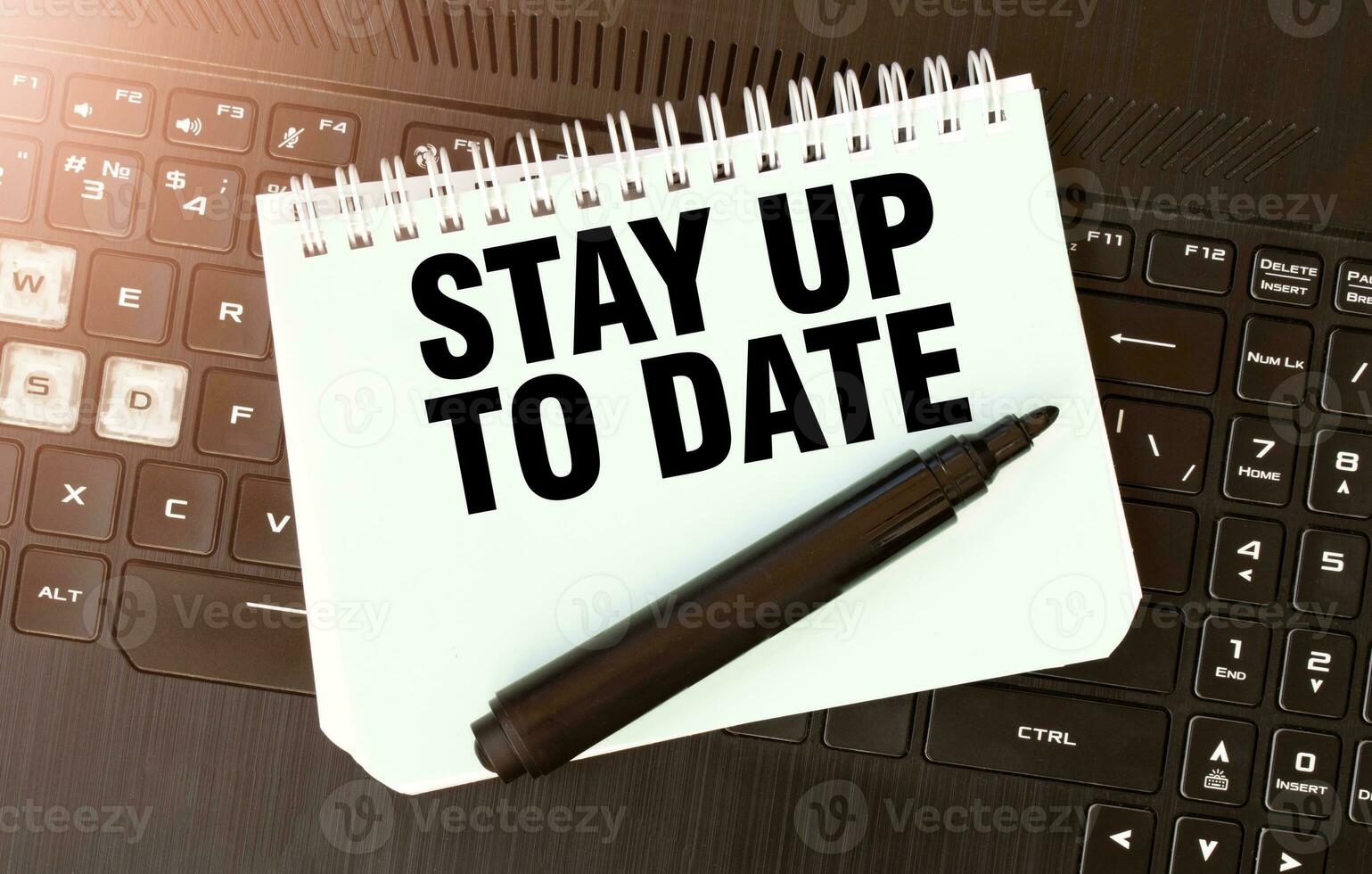 White paper sheet with text STAY UP TO DATE on the black laptop photo