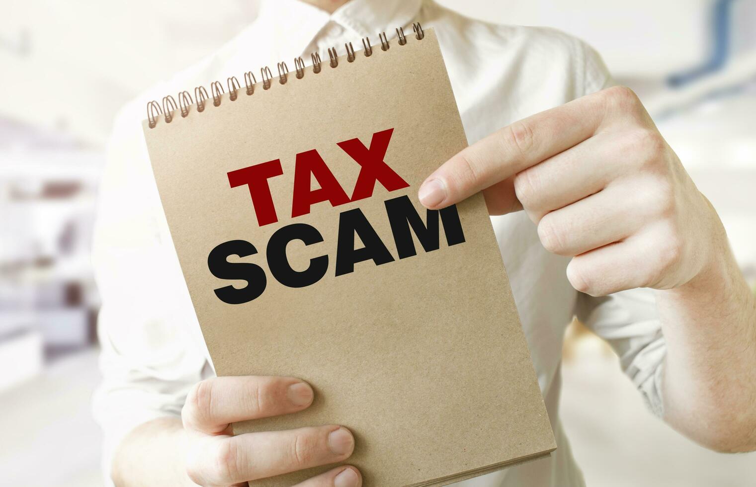 Text TAX SCAM on brown paper notepad in businessman hands in office. Business concept photo