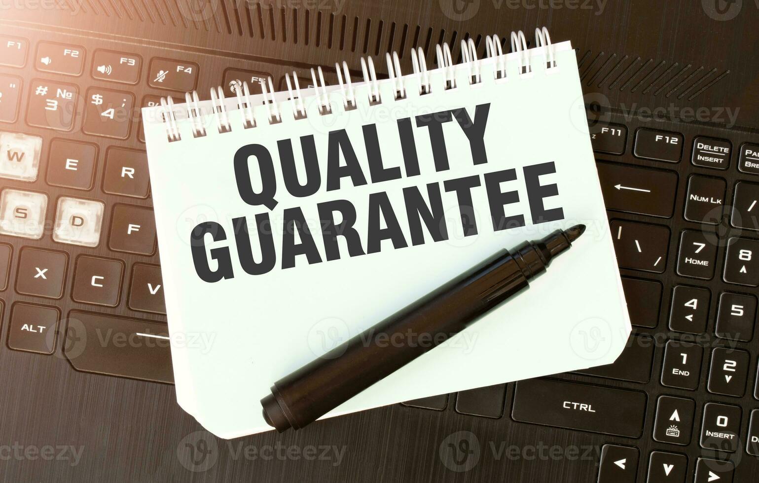 White paper sheet with text QUALITY GUARANTEE on the black laptop photo