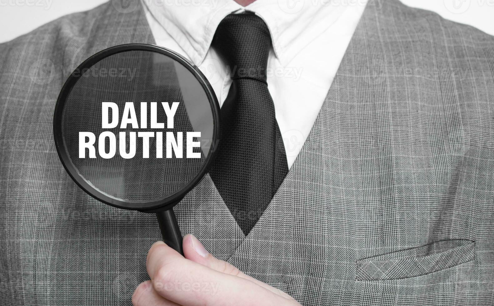 DAILY ROUTINe word on magnifying glass and hand photo