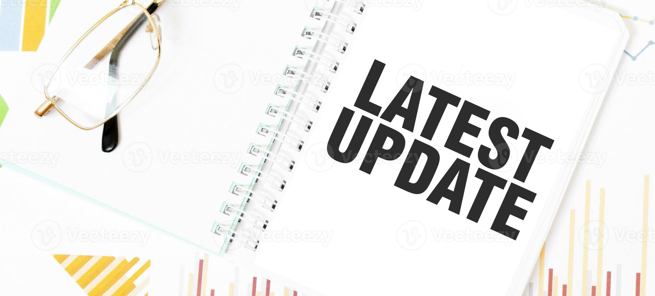 Text LATEST UPDATE on white notepad, glasses, graphs and diagrams. photo