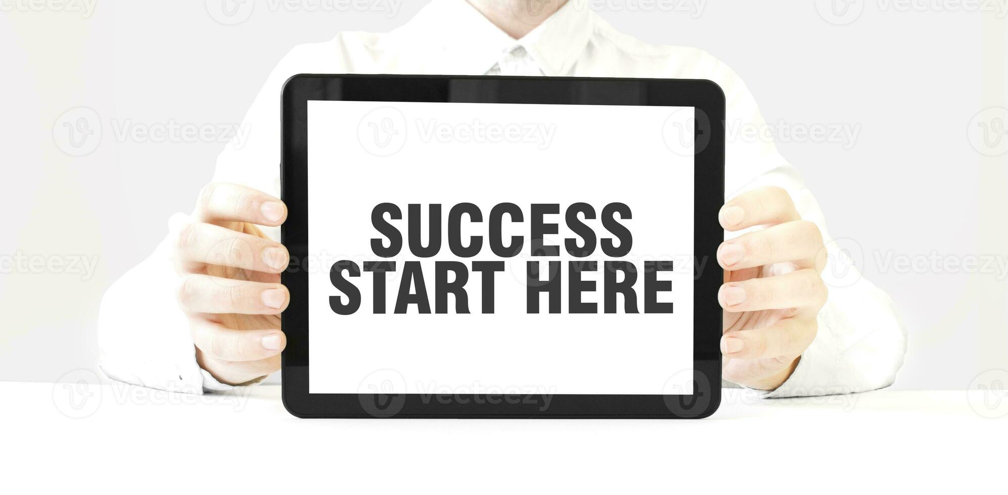 Text SUCCESS START HERE on tablet display in businessman hands on the white background. Business concept photo