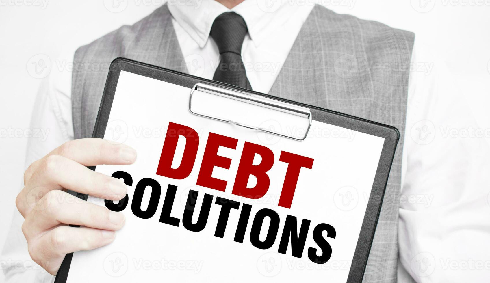 DEBT SOLUTIONS inscription on a notebook in the hands of a businessman on a gray background, a man points with a finger to the text photo