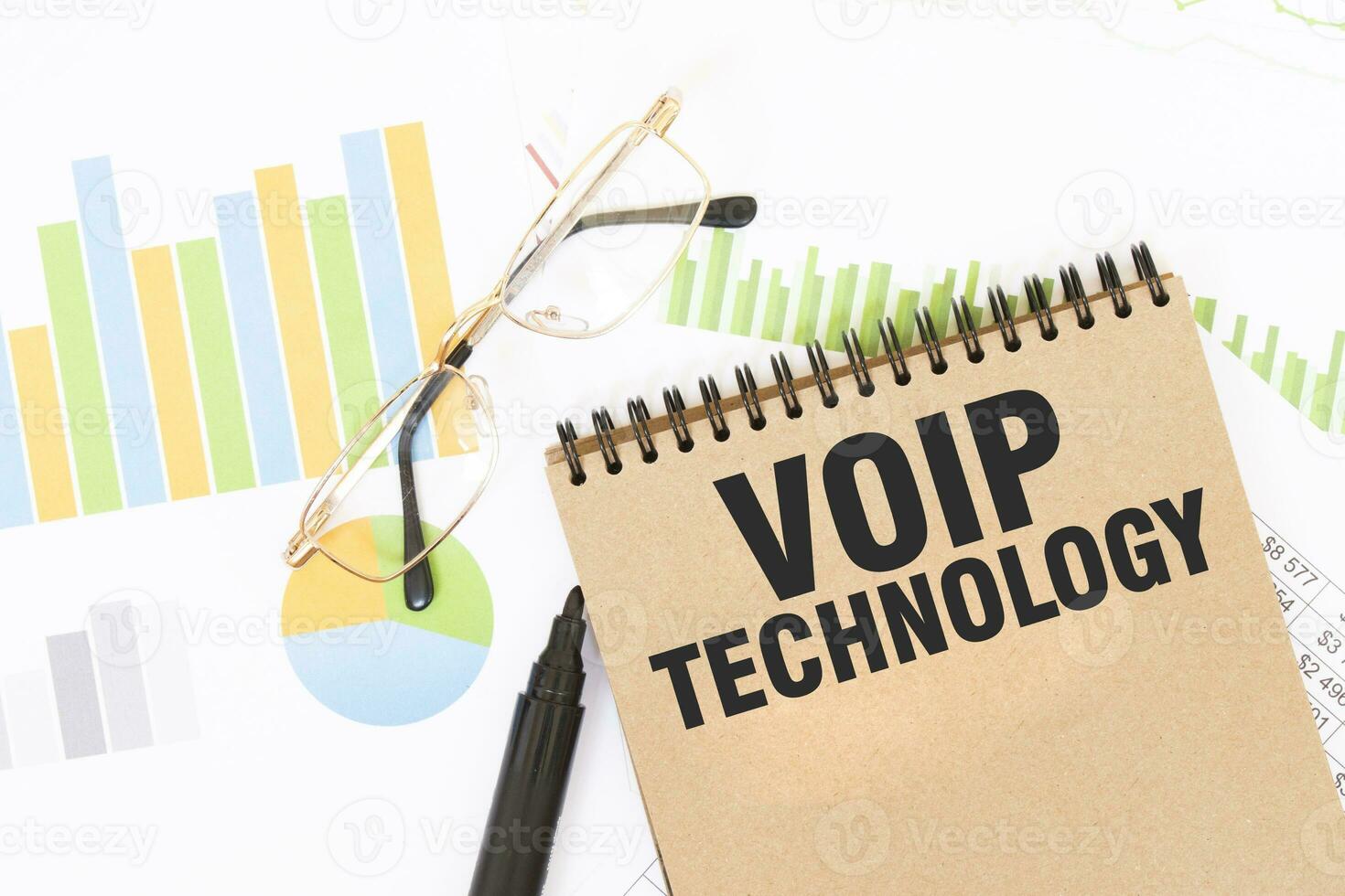 In a craft colour notebook is a VOIP TECHNOLOGY inscription, next to pencils, glasses, graphs and diagrams. photo