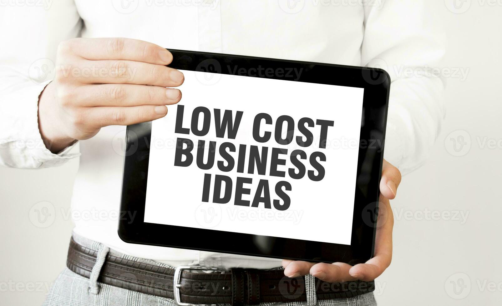 Text LOW COST BUSINESS IDEAS on tablet display in businessman hands on the white background. Business concept photo