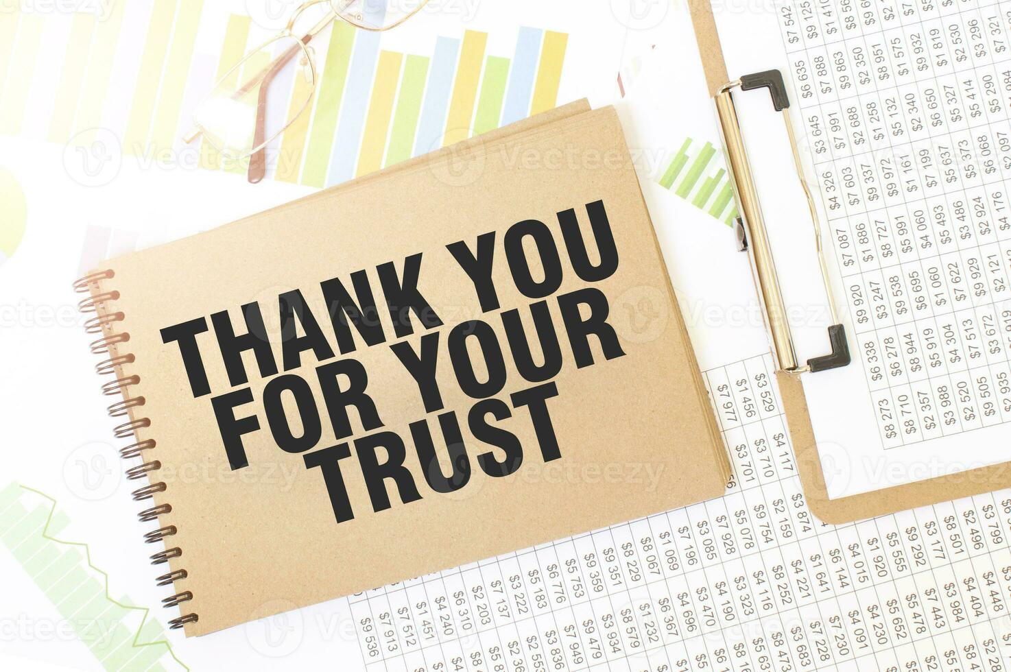 Business up graph on a sheet of craft colour Notepad with THANK YOU FOR YOUR TRUST. sign. Notepad on desk with financial documentation photo