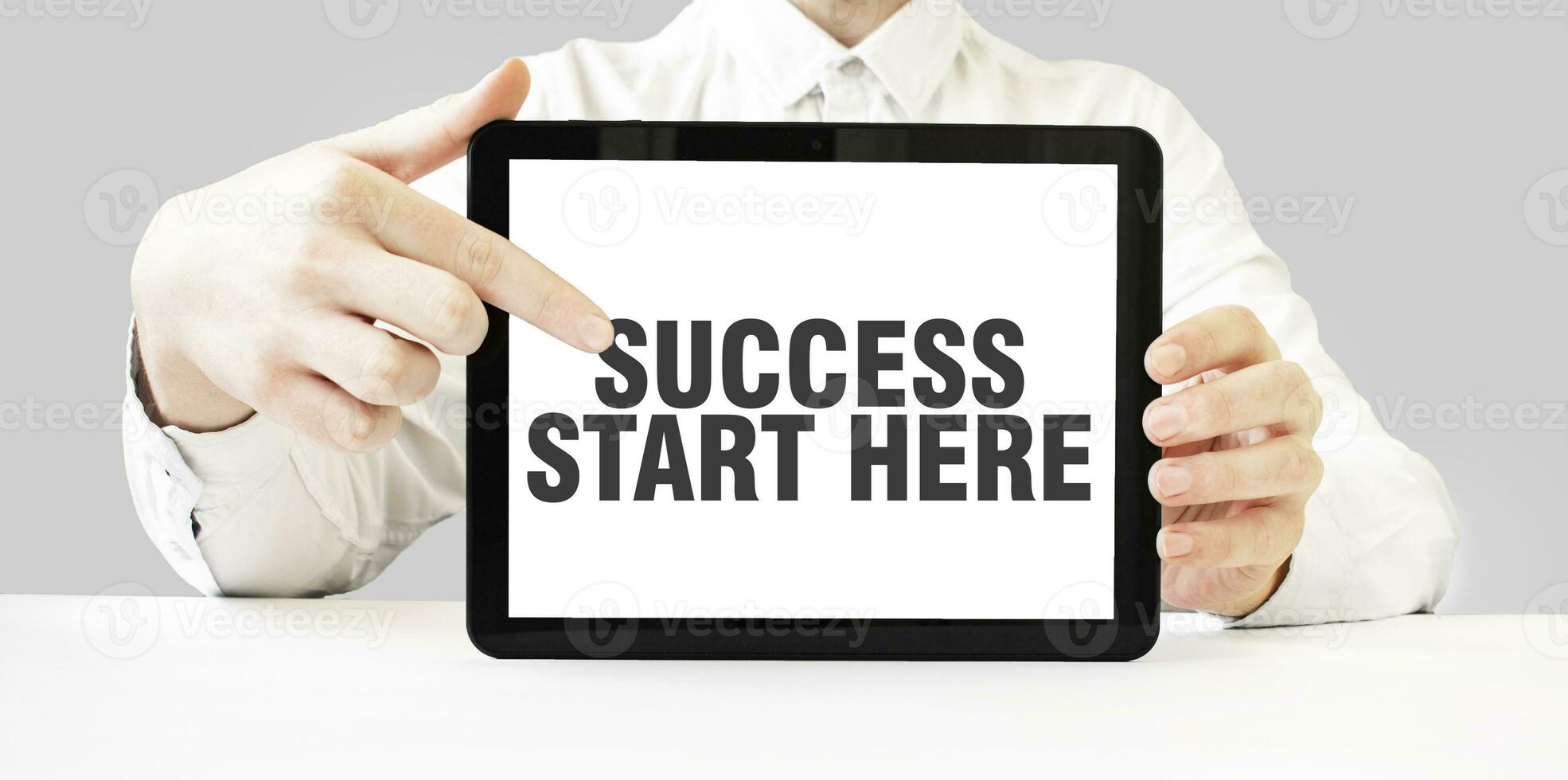 Text SUCCESS START HERE on tablet display in businessman hands on the white background. Business concept photo