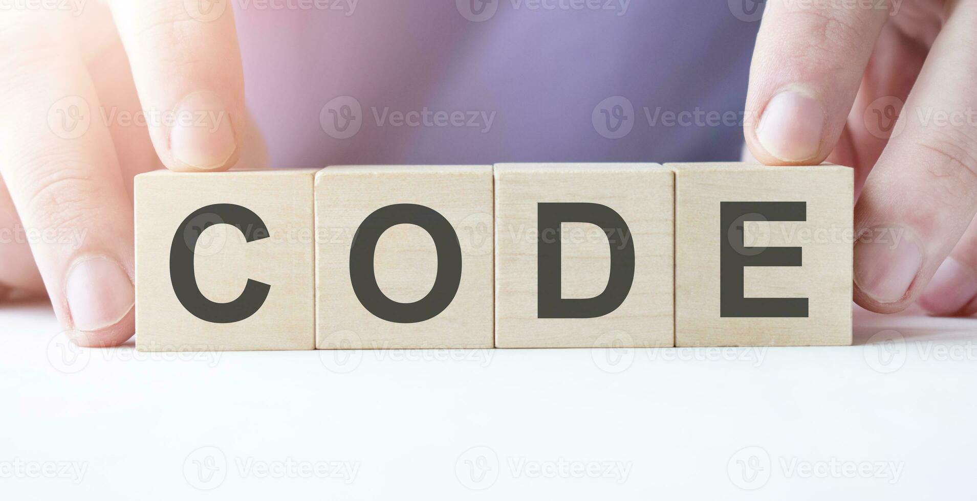 Businessman hand holding wooden cube block with CODE business word on table background. photo