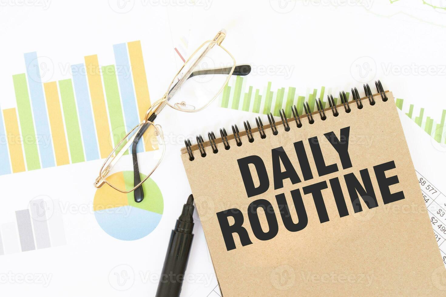 In a craft colour notebook is a DAILY ROUTINE inscription, next to pencils, glasses, graphs and diagrams. photo