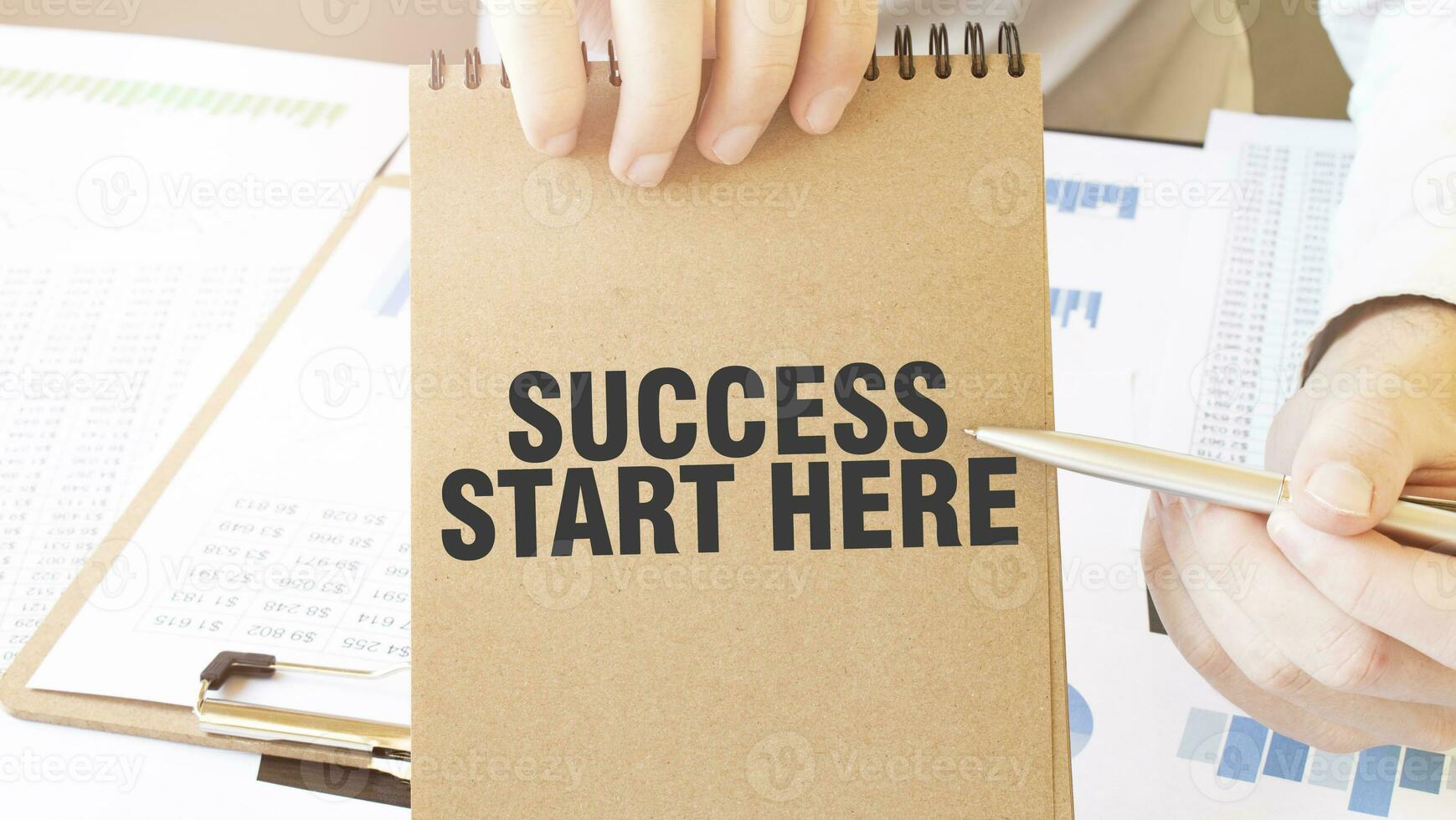 Text SUCCESS START HERE on brown paper notepad in businessman hands on the table with diagram. Business concept photo