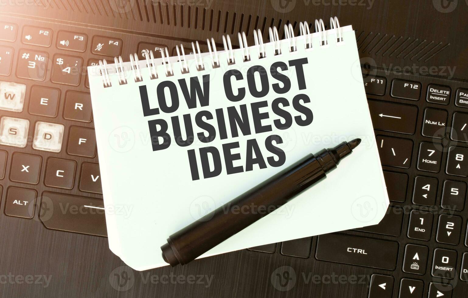White paper sheet with text LOW COST BUSINESS IDEAS on the black laptop photo