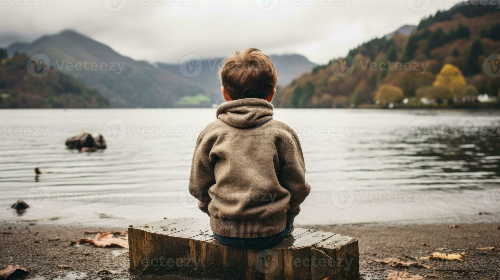 a boy sitting on a log by a lake with mountains in the background generative ai photo