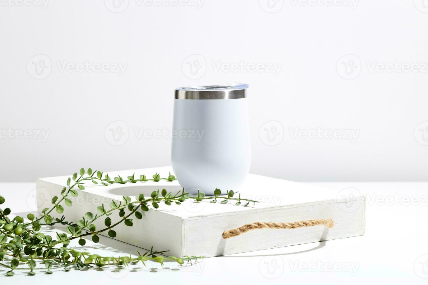 White thermo cup mock up with green plant on wooden tray. Minimal composition to present design. photo
