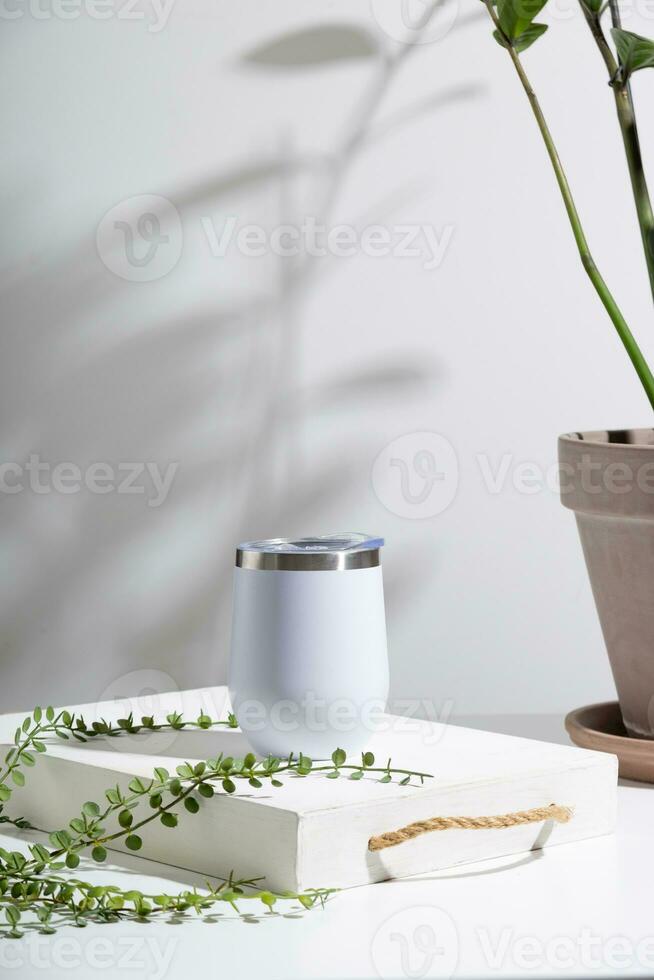 White thermo cup mock up with green plant on wooden tray. Minimal composition to present design. photo