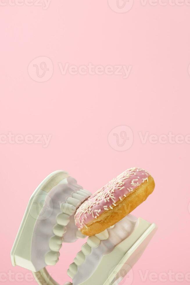 Plastic jaws hold sweet pink donut in teeth. Dental health, dentistry and caries concept. photo