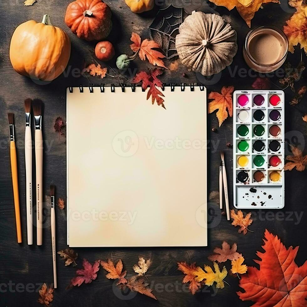 Notebook template on halloween background. White square sketchbook lies on brown wooden table with paints, brushes, halloween pumpkins, orange leaves. Halloween background. Minimalist product mockup. photo