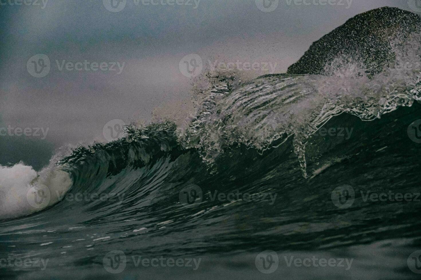 a wave breaking on the ocean with dark blurry sky in background photo