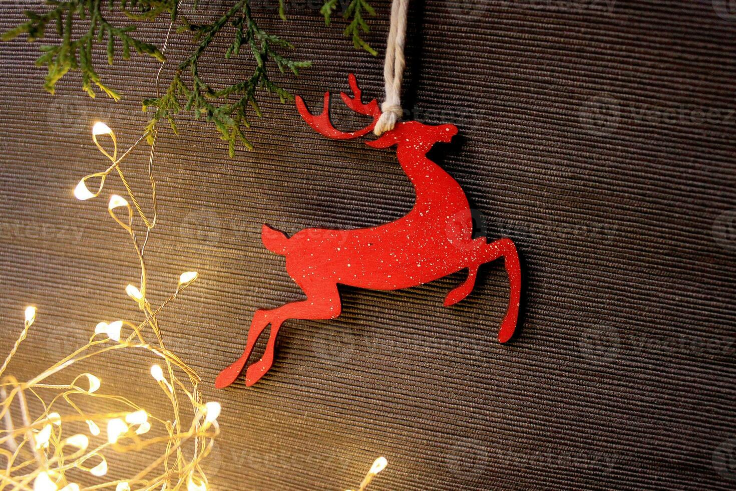 Holiday grey background with coniferous branches, light garland and a wooden figure of a red Christmas deer. Photo with empty space for text and design.