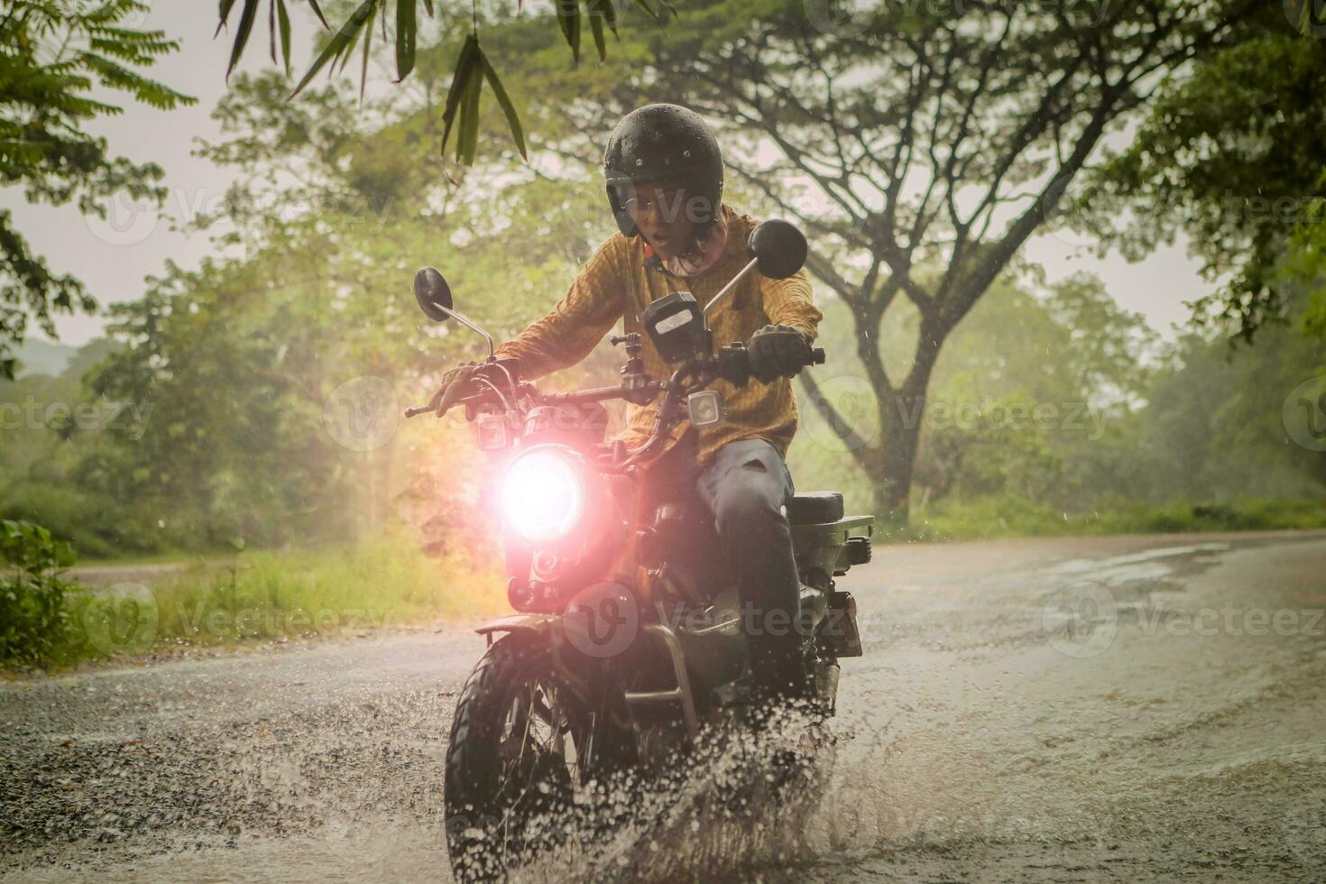 man riding small endurom motorcycle crossing shallow creek among rain falling at forest photo